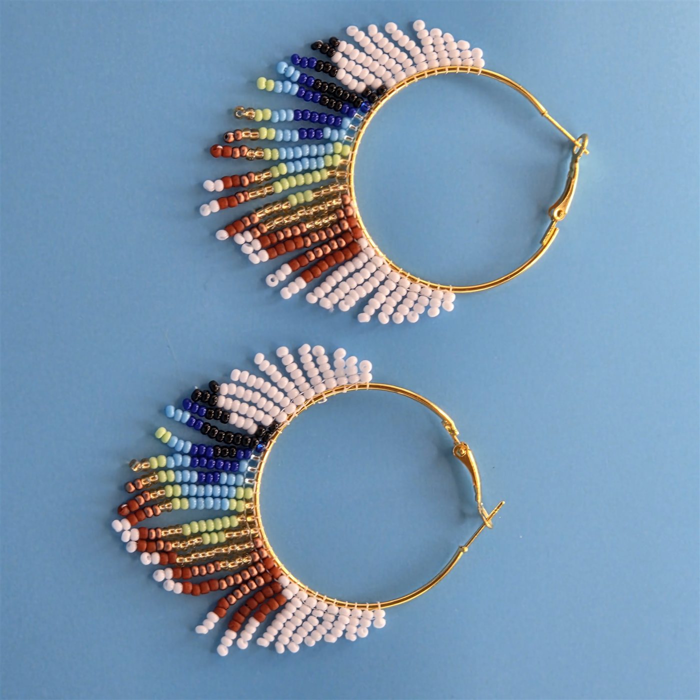 Gold hoop earrings with rainbow handmade beadwork on a blue background